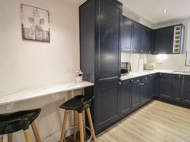 A kitchen with dark blue cabinets a marble countertop a small breakfast bar with two black stools and a wall art of a pig at 21 Taliesin Street in Llandudno