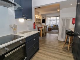 A kitchen with blue cabinets and marble countertop leading to a dining area with table and chairs and a living room with sofa and coffee table at 21 Taliesin Street in Llandudno