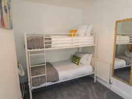 A bedroom with a white metal bunk bed, gray carpet, a wall-mounted mirror, and a colorful painting at 21 Taliesin Street in Llandudno