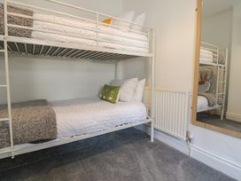 A bedroom with a metal bunk bed with white bedding and pillows a green cushion a radiator and a wall mirror at 21 Taliesin Street Llandudno