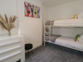 A bedroom with a white bunk bed a white dresser with dried plants in a vase a black stool and a dog painting on the wall at 21 Taliesin Street in Llandudno