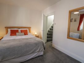 A bedroom with a bed with pillows and blankets a bedside table with a lamp an open door showing carpeted stairs and a mirror on the wall at 21 Taliesin Street in Llandudno