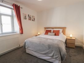 A bedroom with a double bed bedside tables and lamps by a window with red curtains at 21 Taliesin Street in Llandudno