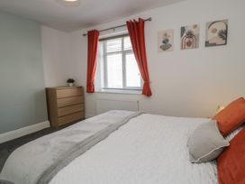 A bedroom with a bed with pillows and blankets a chest of drawers a window with red curtains and three pictures on the wall at 21 Taliesin Street in Llandudno