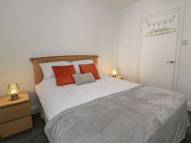 A bedroom with a double bed with white bedding and grey throw and bedside tables with lamps at 21 Taliesin Street in Llandudno