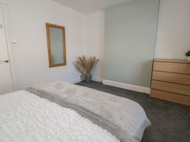 A bedroom with a bed covered in a blanket a wooden dresser a pampas grass arrangement in a vase and a wooden framed mirror on the wall at 21 Taliesin Street in Llandudno