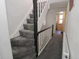 A carpeted staircase with white and black railing next to a hallway with a radiator and doorway leading to another room at 21 Taliesin Street in Llandudno
