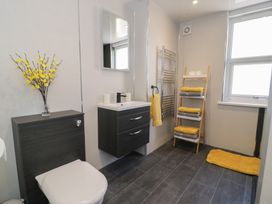 A bathroom with a toilet, a wall-mounted sink, a mirror, a towel rack, a ladder shelf with towels, and a window at 21 Taliesin Street in Llandudno