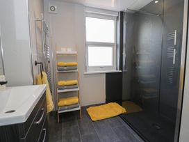 A bathroom with a sink cabinet a towel rack with yellow and gray towels a window and a shower at 21 Taliesin Street in Llandudno