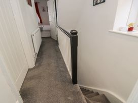 A carpeted upstairs hallway with a black and white railing and a bedroom door open at 21 Taliesin Street Llandudno