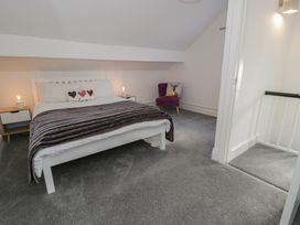 A bedroom with a white bed and nightstands with lamps and a purple chair with a pillow at 21 Taliesin Street in Llandudno
