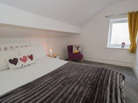 A bedroom with a bed white bedding a side table with a lamp a purple chair a window with yellow curtains and a small plant at 21 Taliesin Street in Llandudno