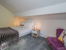 A bedroom with a white bed with heart pillows a nightstand with a lamp and a purple chair with a deer pillow at 21 Taliesin Street in Llandudno