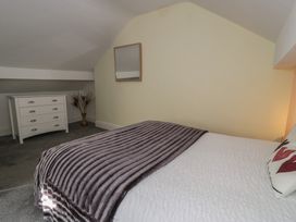 A bedroom with a bed covered with a white quilt and purple blanket a white chest of drawers a mirror on the wall and a vase with dried plants at 21 Taliesin Street in Llandudno