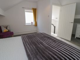 A bedroom with a bed covered by a gray blanket a purple chair with a cushion and a window with yellow curtains at 21 Taliesin Street in Llandudno