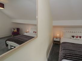 A bedroom with a bed a bedside table with a lamp a purple chair and a mirror on the wall at 21 Taliesin Street in Llandudno