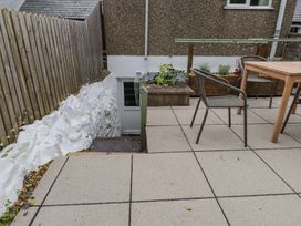 An outdoor patio area with concrete tiles a wooden table two chairs and steps leading to a door at Hafod in Llanbedrog