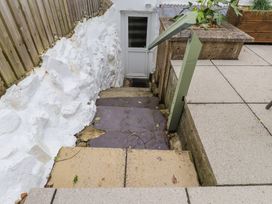 A set of stone steps leading down to a white door with a wooden fence on one side and a concrete wall with plants on the other side at Hafod in Llanbedrog