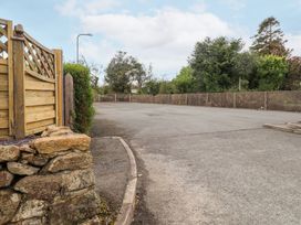 An empty paved parking area with wooden fence and stone wall on the left and trees in the background at Hafod in Llanbedrog