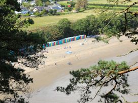 A sandy beach with colorful beach huts people and trees at Hafod in Llanbedrog