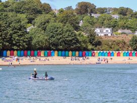 A beach with colorful beach huts and people on the sand and in a small boat on the water at Hafod in Llanbedrog