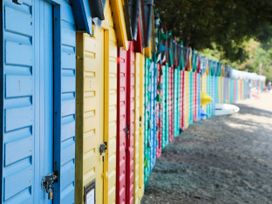 A row of colorful beach huts with padlocked doors on a gravel path with trees on the side