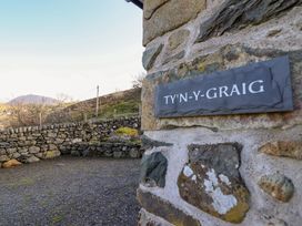 Stone wall with a sign reading TY'N-Y-GRAIG and a stone fence with plants and hills in the background at Tyn Y Graig in Fairbourne