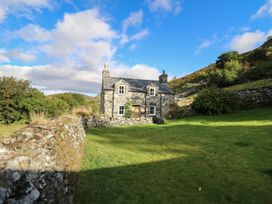 A stone cottage with a slate roof surrounded by a stone wall and green grass at Tyn Y Graig in Fairbourne