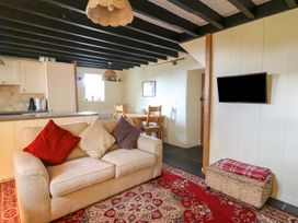 A living room with a beige sofa and three cushions a wall-mounted TV a dining table and chairs at Tyn Y Graig in Fairbourne