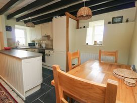 A kitchen and dining area with wooden table and chairs and white cabinets at Tyn Y Graig in Fairbourne