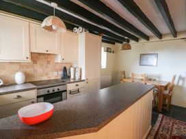 A kitchen with cabinets stove and dining table with chairs at Tyn Y Graig in Fairbourne