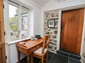 A wooden desk and chair near a window in a room with stone walls and a wooden door at Tyn Y Graig in Fairbourne