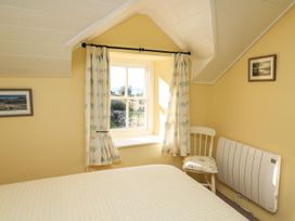 A bedroom with a bed a window with curtains a chair and framed pictures on walls at Tyn Y Graig in Fairbourne