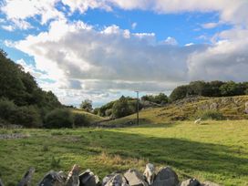 A grassy field with scattered rocks trees and a sheep under a blue sky with clouds at Tyn Y Graig in Fairbourne