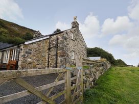 A stone house with a wooden fence and gate next to a grassy field at Tyn Y Graig in Fairbourne