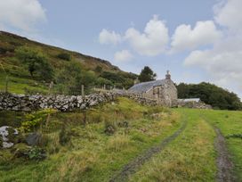 A dirt path leading to a stone house with fenced stone walls in a grassy hillside area at Tyn Y Graig in Fairbourne
