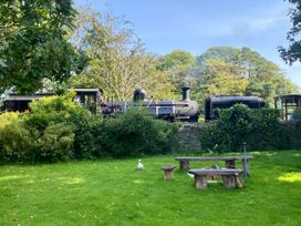 A steam train passing through a garden with a duck and seating area at Garden Flat in Porthmadog