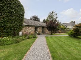 A gravel path leading to a stone building with green lawns and trees at Mistletoe Cottage in Kemeys Commander near Usk