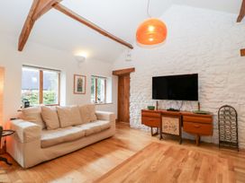 A living room with a beige sofa and a wooden cabinet with a TV on a stone wall at Mistletoe Cottage in Kemeys Commander near Usk