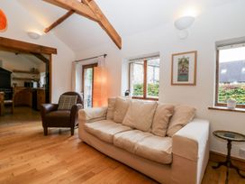 A living room with a beige couch and a brown armchair near windows and a lamp at Mistletoe Cottage in Kemeys Commander near Usk
