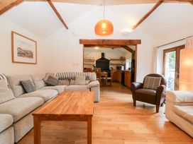 A living room with a wooden coffee table a grey sectional sofa a brown armchair and an open doorway to a kitchen at Mistletoe Cottage in Kemeys Commander near Usk