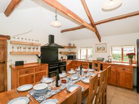 A kitchen with wooden cabinets a black stove a wooden dining table set with plates wine glasses and bottles at Mistletoe Cottage in Kemeys Commander near Usk
