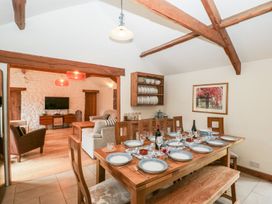 A dining area with a wooden table set for ten and an adjoining living room with sofas and a television at Mistletoe Cottage in Kemeys Commander near Usk
