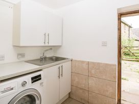 A utility room with a washing machine a stainless steel sink a countertop white cabinets tiled walls and an open door to an outdoor area at Mistletoe Cottage in Kemeys Commander near Usk