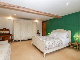 A bedroom with a bed with floral bedding green paneled wall white wardrobe wooden desk and armchair at Mistletoe Cottage in Kemeys Commander near Usk