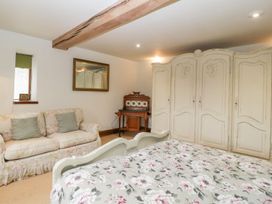 A bedroom with a floral bedspread a floral sofa a large wardrobe and a wooden writing desk at Mistletoe Cottage Kemeys Commander near Usk