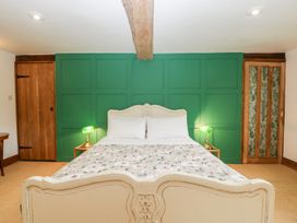 A bedroom with a white bed and floral bedding against a green paneled wall with two bedside lamps at Mistletoe Cottage in Kemeys Commander near Usk