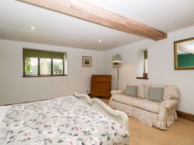 A bedroom with a floral pattern bedspread a floral sofa with cushions a wooden chest of drawers and a floor lamp at Mistletoe Cottage Kemeys Commander near Usk