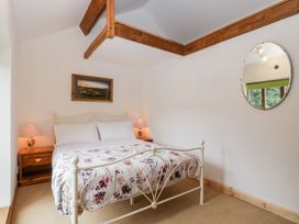 A bedroom with a white metal bed frame two bedside tables with lamps a wall mirror and exposed wooden ceiling beams at Mistletoe Cottage in Kemeys Commander near Usk