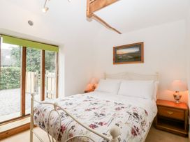 A bedroom with a white metal bed frame floral bedspread wooden bedside tables lamps and a large window at Mistletoe Cottage in Kemeys Commander near Usk